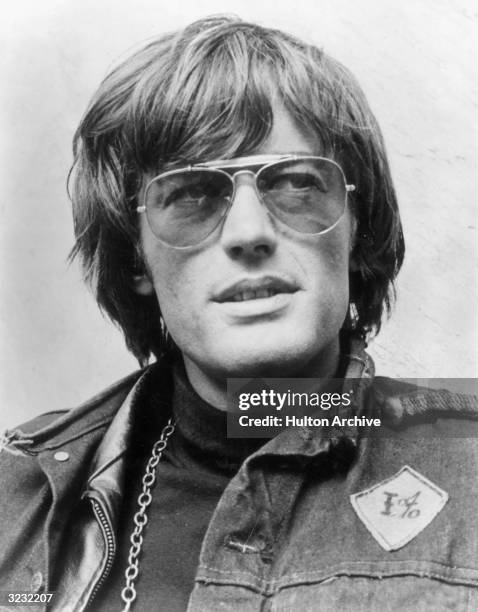 Outdoor headshot of American actor, screenwriter and producer Peter Fonda, wearing sunglasses and a denim jacket. He wears a metal chain and a...