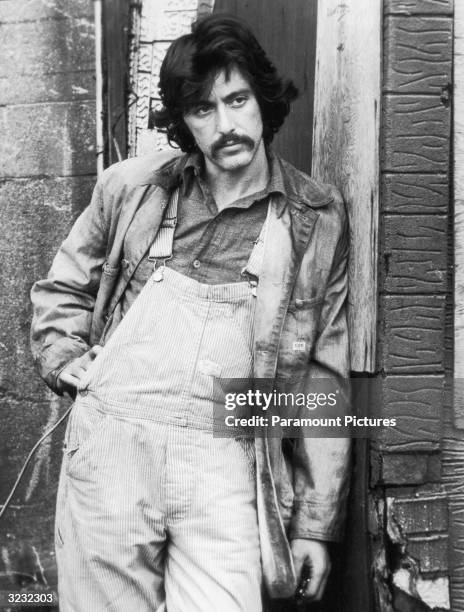 American actor Al Pacino leans against a building, wearing overalls and a work coat, in a still from director Sidney Lumet's film, 'Serpico'. The...