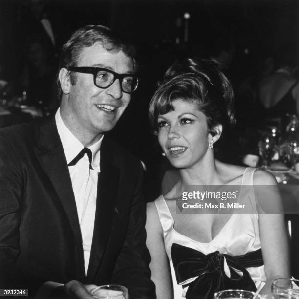 British actor Michael Caine sits next to American singer and actor Nancy Sinatra at the premiere party for Martin Ritt's film, 'The Spy Who Came in...