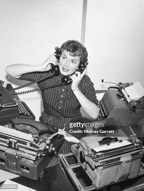 American actor Barbara Hale holds two telephones to her ears while surrounded by four typewriters, posing as the hardworking poster girl for National...