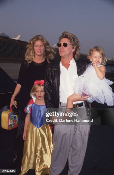 British rock star Rod Stewart standing in an airport parking lot holding hands with his daughter, Ruby , and carrying his daughter Renee at his hip,...