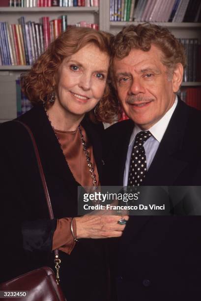 Married American comedians and actors Anne Meara and Jerry Stiller embracing in front of a bookshelf.