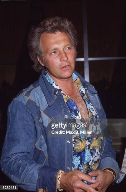 American stunt performer Evel Knievel waits for his car outside the Beverly Hilton Hotel, wearing an open-chested floral shirt and a denim shirt over...