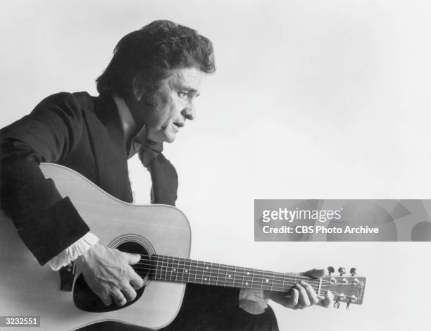 Profile of American country singer Johnny Cash , wearing a tuxedo, playing an acoustic guitar, in a promotional still for the 11th annual Country...