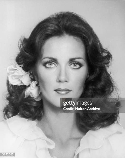 Closeup portrait of American actor Lynda Carter wearing a flower behind her ear and a ruffle-collared shirt.