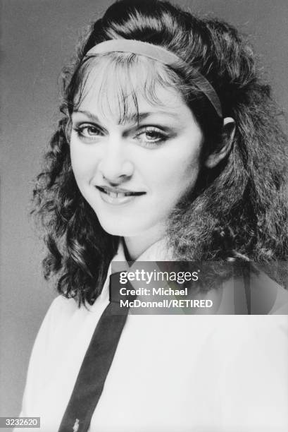 Studio headshot portrait of future American pop singer Madonna smiling while wearing a white cotton shirt with a dark tie, New York City. She wears a...