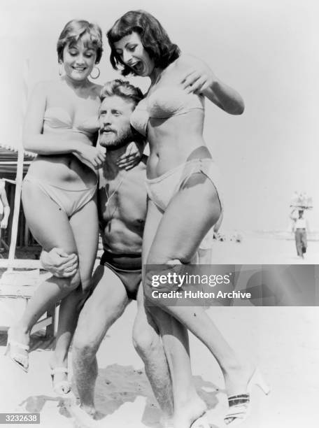 American actor Kirk Douglas, wearing a swimsuit, lifts two women wearing bikinis on a beach during the Venice Film Festival, Italy.