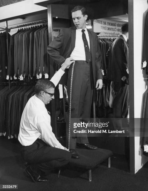 Tailor uses a tape measure to measure a man's pants for alterations, in a men's garment store.