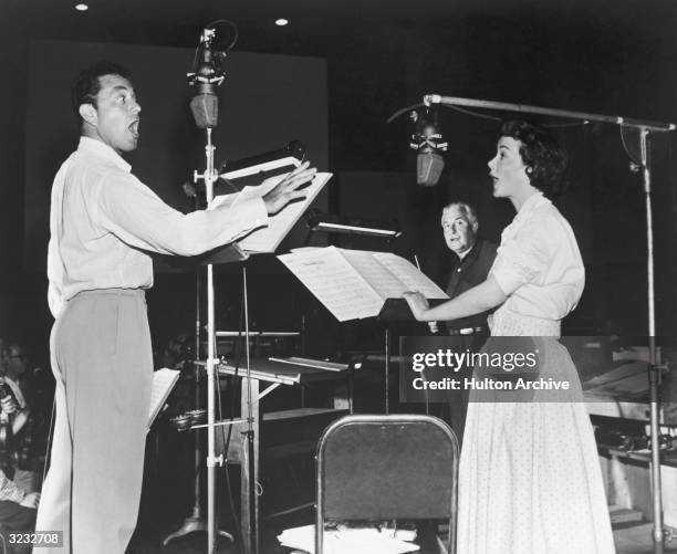 American actors Tony Martin and Kathryn Grayson stand and sing for a radio broadcast, as American conductor Arthur Fiedler stands behind them,...
