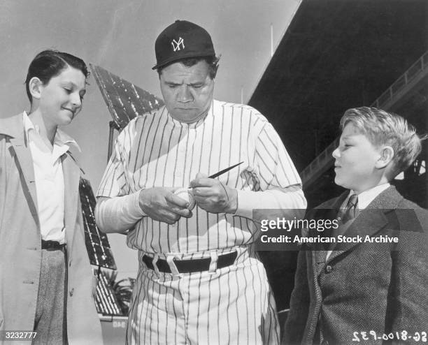 American baseball player Babe Ruth , outfielder for the New York Yankees, autographs a baseball for two young fans.