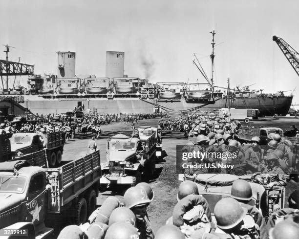 Troops are loaded onto trucks after disembarking from a large transport ship, North Africa.