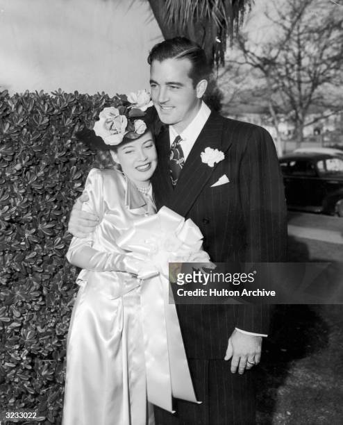American actor Gloria DeHaven smiles with her new husband, actor and singer John Payne, as they stand outdoors after their wedding. She wears a hat...