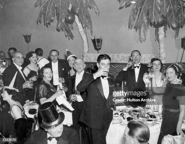 Group of men and women smile at the camera, raising and sipping their glasses of champagne at the stroke of midnight on New Year's Eve at the El...