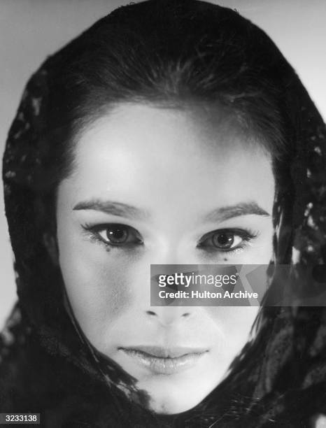 Close-up of American actor Geraldine Chaplin wearing a lace shawl on her head and looking at the camera.