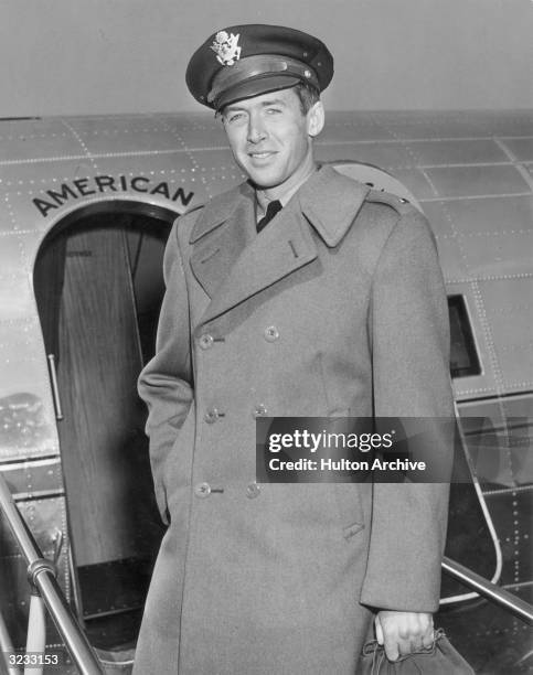 Portrait of American actor Jimmy Stewart in his Air Force cap and wool overcoat, in front of a military airplane.
