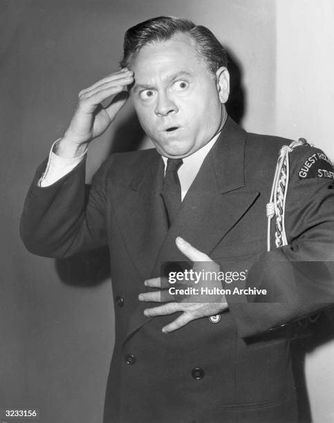 American actor Mickey Rooney, wearing a staff uniform, holds one hand to his chest and the other to his forehead as he makes a distressed facial...