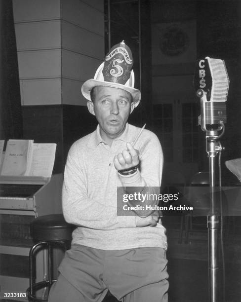 American singer and actor Bing Crosby wearing a firefighter's hat from the American jazz band Firehouse Five during a rehearsal for his show at the...