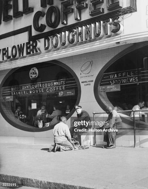 Caucasian officer receives a shoe shine from an African-American youth outside a coffee and doughnut shop, Times Square, New York City