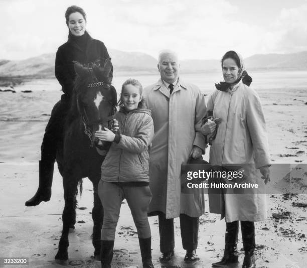 British-born actor and filmmaker Charlie Chaplin stands with his fourth wife Oona and two of his daughters, Geraldine and Jane, outdoors near a lake,...