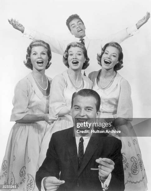 Group promotional portrait of American television personality Dick Clark snapping his fingers to the beat of a song as the McGuire Sisters, made up...