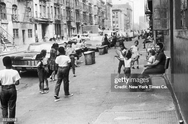 Children play in the street under adult supervision on East 111th Street, between Lexington and Third Avenues in Harlem, New York City.