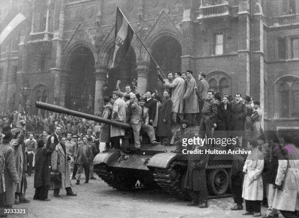 Group of men hold a flag on top of a tank in front of the Parliament building during the Hungarian Revolt, Budapest, Hungary.