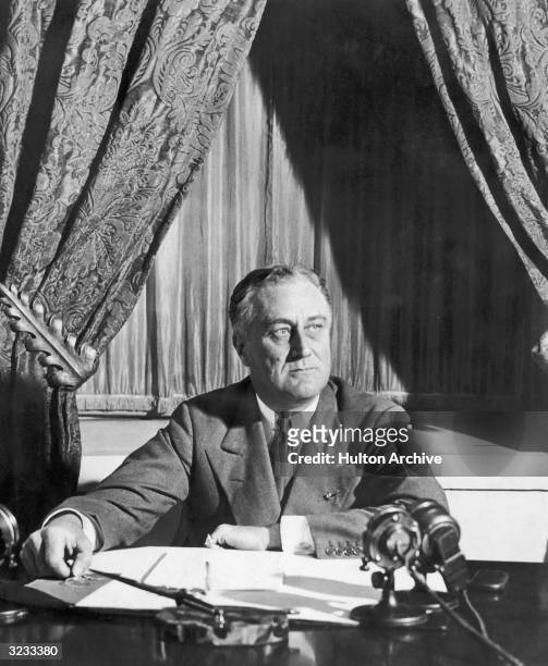 American President Franklin Roosevelt sits at a desk with microphones, probably during a radio broadcast.