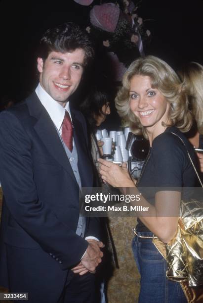 Actors John Travolta and Olivia Newton-John stand at a bar at a party for the film, 'Grease,' in which they both starred. Travolta is wearing a suit...