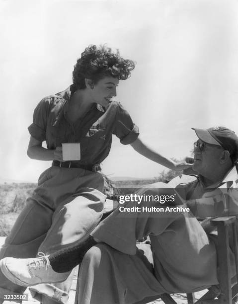 American actor Ava Gardner , holding a coffee mug, talks to American film director John Ford , on the set of the film, 'Mogambo'.