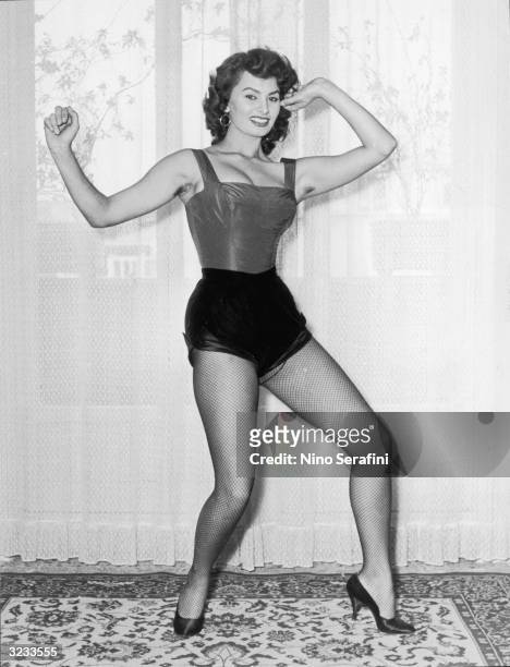 Full-length view of Italian actor Sophia Loren posing in a cabaret costume with fishnet stockings and high heels in front of a window.