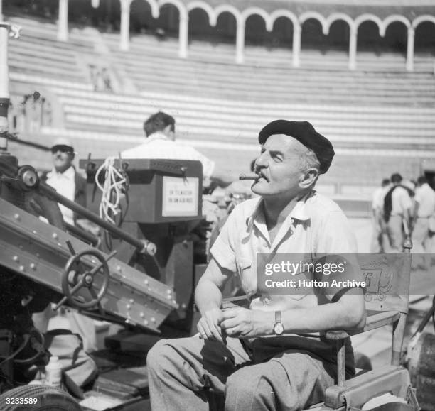 American film executive, producer and screenwriter Darryl F Zanuck smokes a cigar from his director's chair in a bull ring on the set of director...