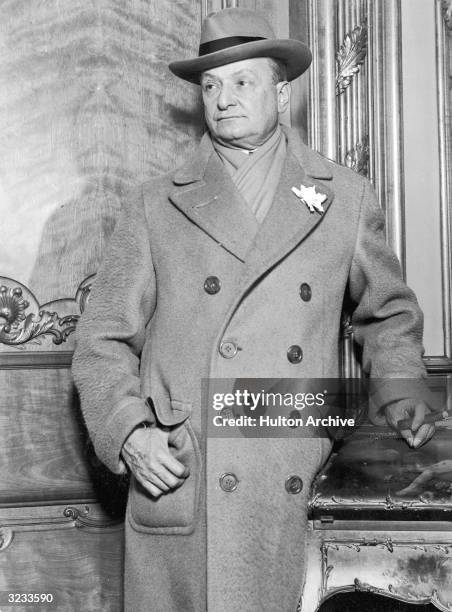 American theatrical producer Florenz Ziegfeld Jr smokes a cigar in a double-breasted overcoat, which bears his trademark white flower in its lapel....