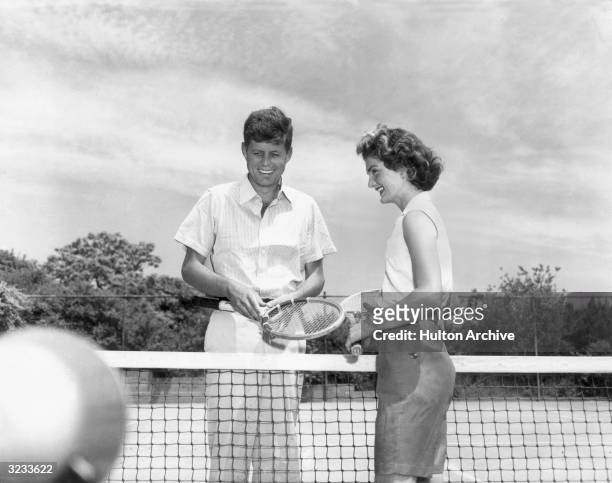 Senator John F Kennedy and his wife, Jacqueline , stand on either side of a tennis net, holding tennis racquets, Hyannis Port, Massachusetts.