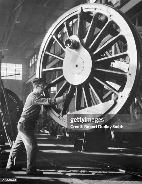 Factory worker helps maneuver an enormous locomotive flywheel into position.