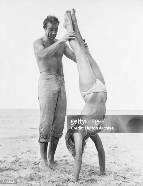 Shirtless Scottish actor Sean Connery holds Swiss actor Ursula Andress while she does a handstand on a beach in a white bikini on the set of the...