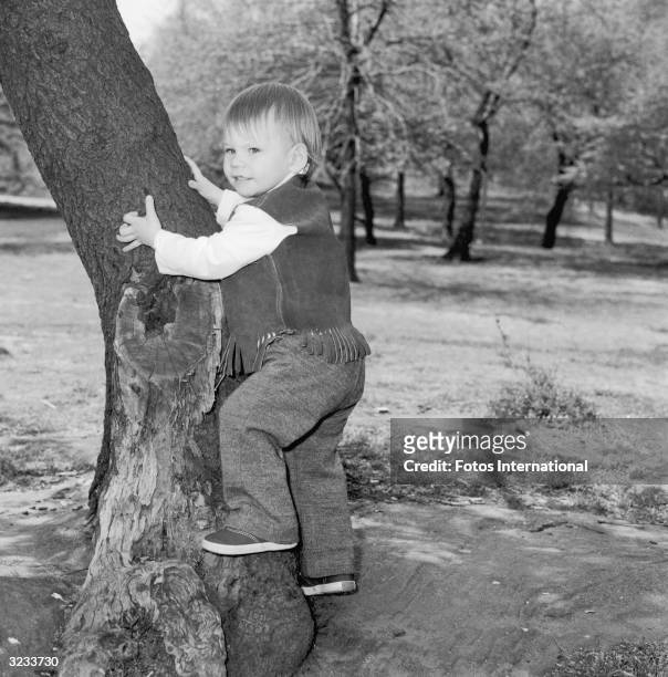 American actor Christian Slater as a toddler, climbing a tree in Central Park, New York City. He is wearing a fringed suede vest.
