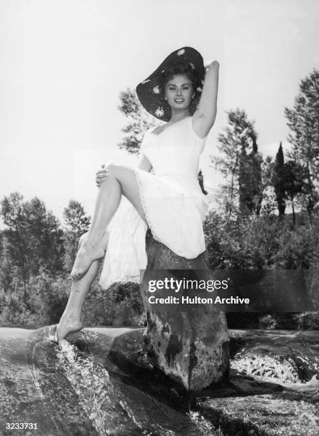 Italian actor Sophia Loren poses barefoot on a rock in a stream in a promotional portrait for the film, 'The Miller's Beautiful Wife', directed by...