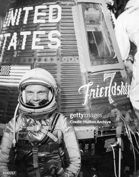 American astronaut John Glenn Jr smiles while wearing a spacesuit and helmet in front of the Mercury Atlas 6 spacecraft 'Friendship 7', Cape...