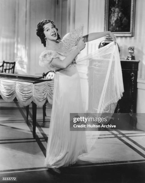 American comedian Fanny Brice sings while fanning herself in a dress with an Empire-waist in an unidentified film still.