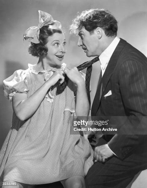 American comedian Fanny Brice , dressed as her young girl persona, Baby Snooks, pulls British actor Hanley Stafford's tie in a promotional portrait...