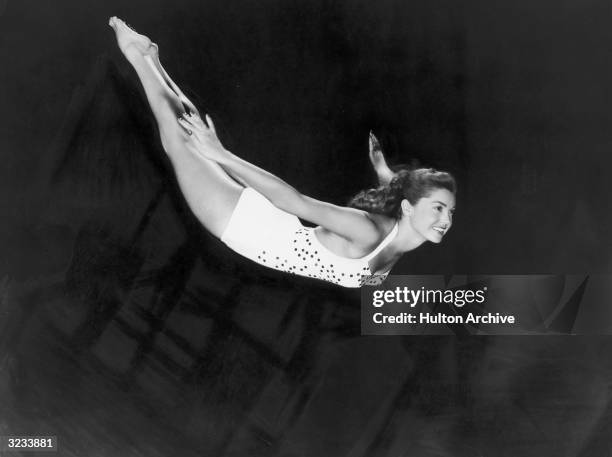 Portrait of aquatic American actor and swimmer Esther Williams diving through the air in a one-piece swimsuit.