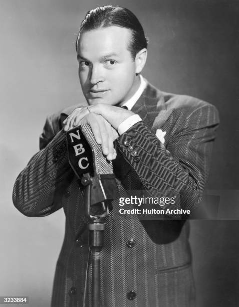 Promotional portrait of British-born entertainer Bob Hope wearing a herringbone suit and posing with his hands over an NBC radio microphone.