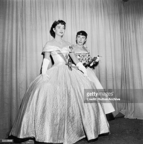American costume designer Edith Head holds her Oscar as actor Marla English models the ball gown Head designed for Audrey Hepburn to wear in director...