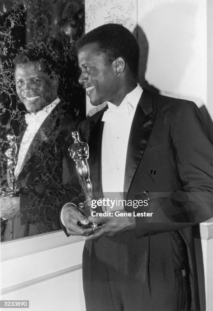 American actor Sidney Poitier looks into a mirror and smiles while holding his Best Actor Oscar for director Ralph Nelson's film, 'Lilies of the...
