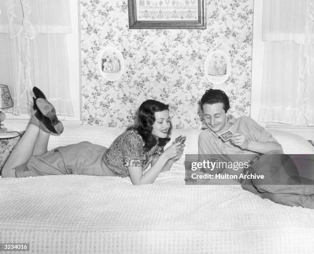 American actor Gene Tierney sits on an eight foot-square bed next to her husband, French-born fashion designer Oleg Cassini, as they play gin rummy.