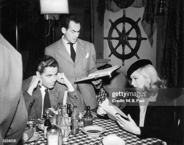 Canadian actor Glenn Ford sits next to American actor Claire Trevor as they rehearse dialogue with Michael Gordon for director Sidney Salkow's film,...