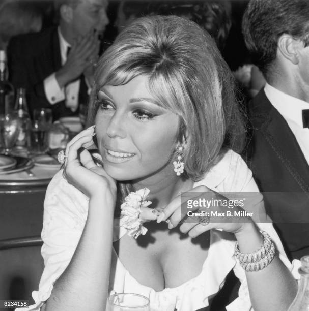 Headshot of American actor and singer Nancy Sinatra sitting and holding a flower at a Cocoanut Grove opening, Los Angeles, California. She is wearing...