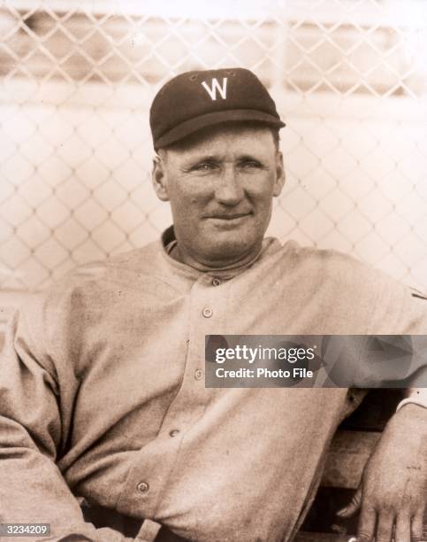 Headshot portrait of American baseball pitcher Walter Johnson , of the Washington Nationals, leaning on a bench.