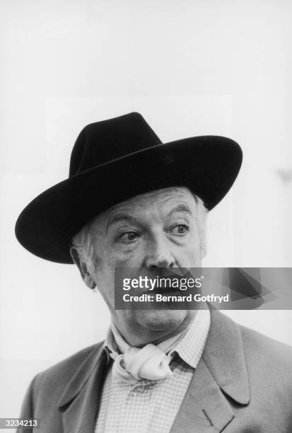 Headshot of British fashion photographer and designer Cecil Beaton wearing a hat and an ascot.