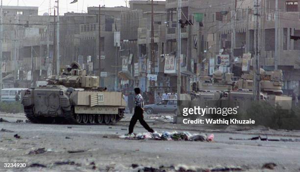 An Iraqi youth crosses behind retreating U.S. Armored personnel carriers April 6, 2004 in the sprawling Shia slum known as Sadr City in Eastern...